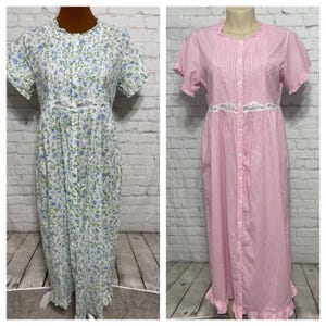 May include: Two vintage nightgowns. One is white with a blue floral pattern, short sleeves, and a ruffled neckline. The other is pink and white striped with short sleeves, a button-down front, and a ruffled neckline. Both have a lace detail at the waist.