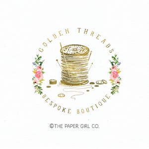 Könnte beinhalten: Goldenes Logo mit dem Text "Golden Threads Bespoke Boutique" und dem Copyright-Symbol gefolgt von "The Paper Girl Co.". Das Logo zeigt eine Garnrolle mit Nadeln und Knöpfen, umgeben von rosa und weißen Blumen.