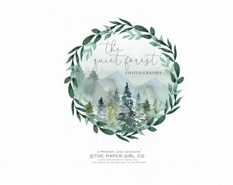 May include: A watercolor logo design featuring a wreath of green leaves surrounding a mountain scene with pine trees. The text "the quiet forest photography" is written in a cursive font.