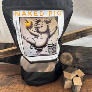 Op de afbeelding: Een zwarte zak met een wit label waarop "NAKED PIG" staat en een cartoon varken met een appel. Het label vermeldt ook "PARR'S BBQ SMOKING NATURAL WHITE OAK FIREWOOD" en "PARRWOODPRODUCTS.COM". De zak is gevuld met kleine stukjes hout.