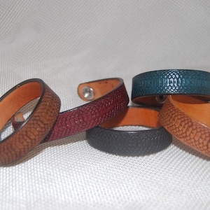 Peut inclure: Cinq bracelets en cuir de différentes couleurs, dont le marron, le bordeaux, le bleu sarcelle et le noir. Chaque bracelet présente un motif texturé en forme de serpent et une fermeture à pression argentée.