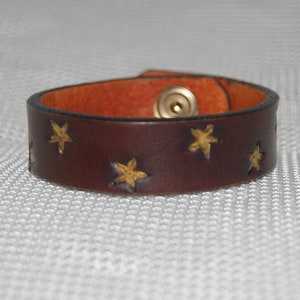 Peut inclure: Un bracelet en cuir marron avec des accents d'étoiles dorées et une fermeture à pression en laiton.