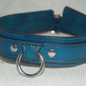Pode incluir: Uma coleira de couro azul-petr&oacute;leo com um anel e rebites de metal prateado. A coleira tem um design arredondado com uma borda preta. O anel de metal &eacute; preso a uma se&ccedil;&atilde;o refor&ccedil;ada.