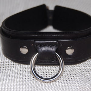 Op de afbeelding: Zwarte leren choker met een zilveren ring en twee zilveren drukknopen.