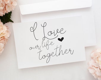 May include: A white greeting card and envelope with the text "I Love our life together" in black script. The card is accompanied by light pink hydrangea flowers.