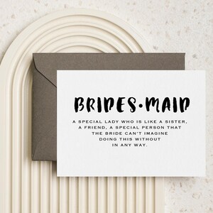 May include: A white card with black text that reads "BRIDES-MAID" and a definition of the word. The card is sitting on a brown envelope.