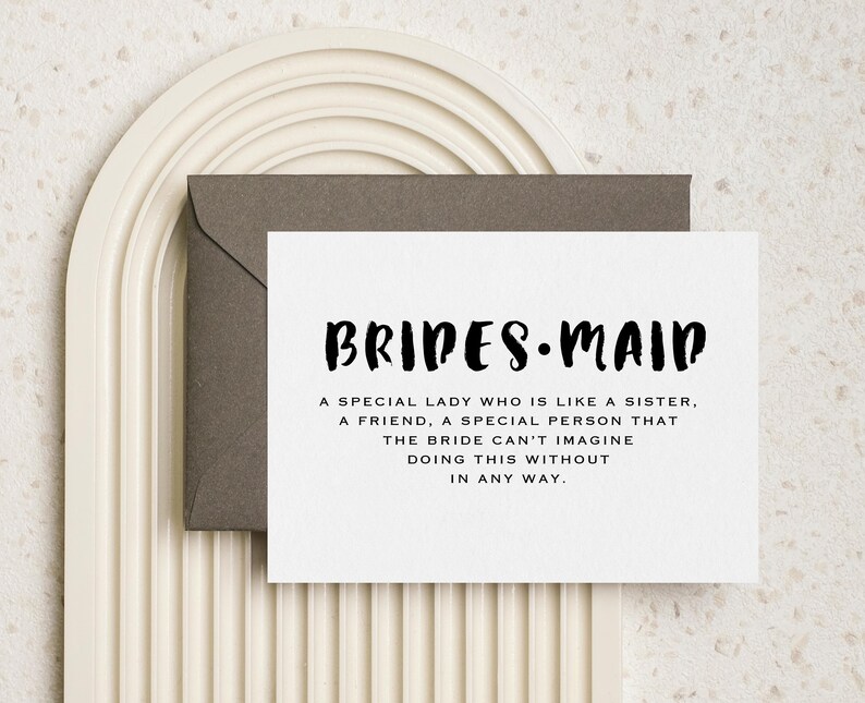 May include: A white card with black text that reads "BRIDES-MAID" and a definition of the word. The card is sitting on a brown envelope.