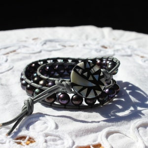 May include: A gray leather wrap bracelet with a black and white geometric patterned button and black pearls.