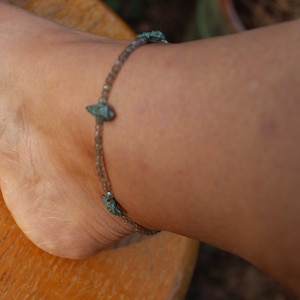 May include: A silver anklet with turquoise-colored stones. The anklet is on a person's ankle.