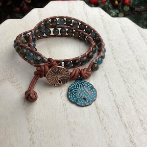 May include: Wrap bracelet with blue and brown beads, brown leather, and a copper-colored button clasp. A turquoise starfish charm hangs from the bracelet. The bracelet is designed to wrap around the wrist multiple times.