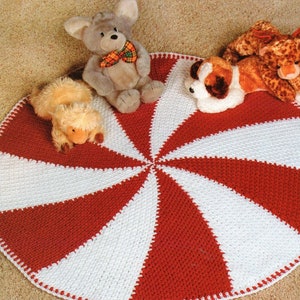 May include: A red and white crocheted round rug with a swirl pattern. Three stuffed animals are sitting on the rug: a gray bunny, a brown and white dog, and a brown and yellow giraffe.