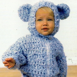 Può includere: Una giacca con cappuccio blu chiaro per neonati, con chiusura a zip e due grandi accenti rotondi a forma di orecchio sul cappuccio. La giacca è realizzata in un materiale strutturato e soffice. Il bambino indossa un capo rosa chiaro.