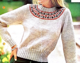 May include: A light beige sweater with a high neckline and long sleeves. The sweater features a patterned yoke in red, black, and white. The ribbed cuffs and hemline provide a fitted look. The sweater is paired with green trousers.