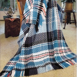 May include: A woven blanket with a plaid design in shades of blue, white, black, and red. The blanket has a fringed edge and is draped over a wooden chair. The blanket's design features a mix of solid and patterned sections.