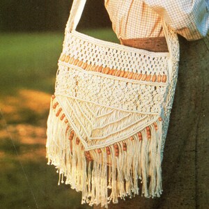 Peut inclure: Sac à bandoulière en macramé crème avec une longue sangle. Le sac présente un motif géométrique, des perles en bois et un fond à franges. Le sac est fait d'un matériau tissé et est de style bohème.