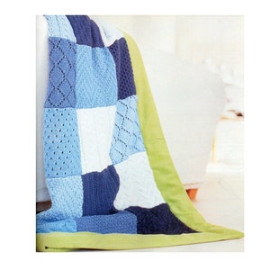 Könnte beinhalten: Eine Patchwork-Decke in Blau- und Weißtönen mit einem grünen Rand. Die Decke weist verschiedene Strickmuster auf, darunter Zopf- und Rautenmuster. Die Decke ist über eine weiße Oberfläche drapiert.