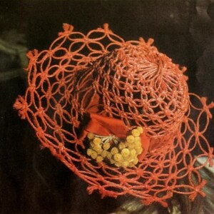 May include: A bright orange crochet hat featuring an openwork lattice pattern throughout the crown and brim. A wide orange ribbon band encircles the base of the crown, accented with a cluster of small, round, yellow decorative floral elements.