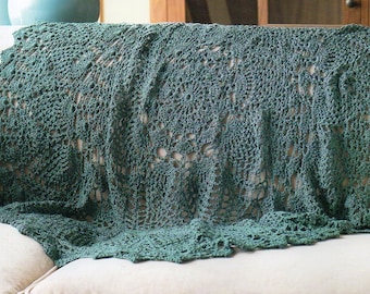 May include: A green crocheted throw blanket with a lacy pattern, draped over a white couch.
