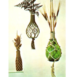 May include: Three macrame plant hangers with dried flowers and greenery. One brown macrame holder contains dried flowers, another green glass bottle is encased in a white macrame holder with wheat stalks, and a third macrame holder contains ferns.