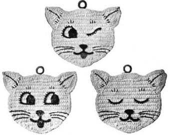 May include: Three crocheted cat face ornaments in a grayscale palette. Each cat face has a different expression: winking, wide-eyed, and sleeping. The ornaments have a small loop at the top for hanging.