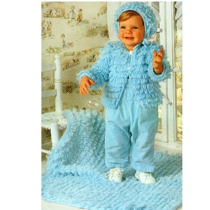 May include: A baby wearing a light blue knitted jacket, pants, and hat. The jacket and hat have a fluffy texture. The baby is standing on a light blue blanket.