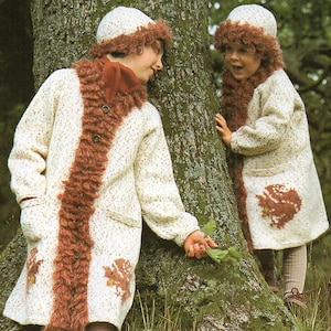May include: Two children wearing matching cream-colored knitted coats with brown fur trim and matching hats. The coats feature a leaf design on the pockets and are buttoned down the front. The children are standing near a tree.