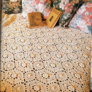 May include: A cream-coloured, crocheted bedspread with a floral pattern, alongside floral pillows and two vintage books. The bedspread has a detailed, openwork design, creating a textured appearance. The books are titled "A Girl of the Limberlost" and "Freckles".