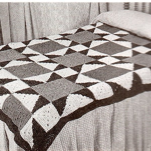 May include: A black and white crocheted throw blanket with a star pattern. The blanket is on a bed with a white and black checkered bedspread.