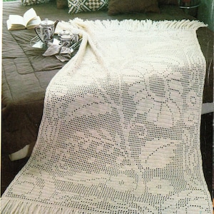 May include: Cream-colored, open-weave crochet blanket with a floral pattern and fringe. The blanket is draped over a bed with decorative pillows and a tea set on a tray.