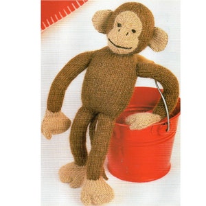 May include: A brown knitted monkey toy with long arms and legs, holding a red bucket. The monkey has a brown face with a stitched smile and black eyes.