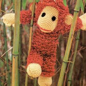 May include: A crocheted monkey toy with red and yellow yarn. The monkey is hanging from bamboo stalks.