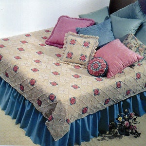 May include: A crocheted bedspread with a rose pattern in pink and white. The bedspread is on a bed with a blue bed skirt and several decorative pillows in pink, blue, and floral patterns.