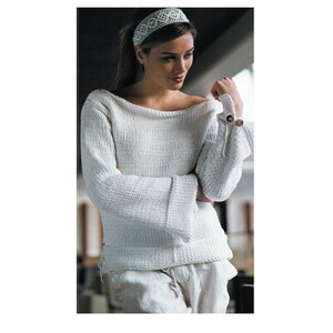 May include: A white knit sweater with a wide neckline and long, flared sleeves. The sleeves are gathered at the wrist and fastened with two round, gold-colored buttons. The model is also wearing a white headband and white pants.