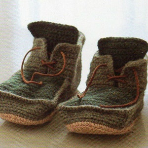 May include: A pair of handmade baby booties. The booties are crocheted with green and brown yarn, featuring a lace-up design with brown laces. The soles are a light pink color. The booties are designed to look like miniature boots.