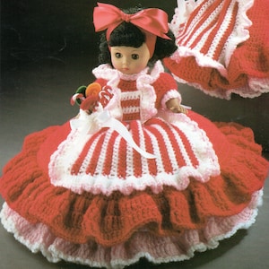 May include: A vintage doll dressed in a handmade crochet outfit. The doll wears a red and white striped dress with a matching jacket and a large red bow. The crochet work features a ruffled skirt and white trim. The doll holds a small bouquet of colorful candies.