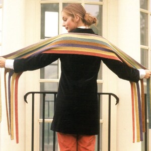 May include: A multi-colored striped scarf with a variety of colors including green, yellow, orange, red, purple, and blue. The scarf is held out, displaying its length and design. The scarf is a fashion accessory.