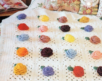 May include: A white crocheted blanket with a repeating pattern of colorful crocheted roses. The roses are in shades of red, orange, yellow, green, blue, purple, and brown.