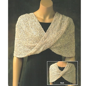 以下が含まれることがあります： クロスデザインのベージュのニットショール。ショールはモデルが着用している様子と、平らに置かれた様子が示されています。