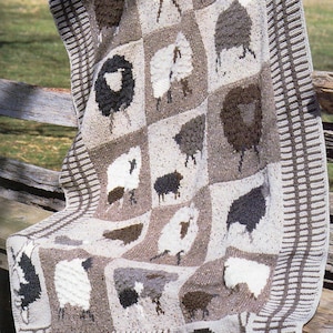 May include: A knitted throw blanket featuring a patchwork design of white and brown sheep. The blanket has a brown and white striped border.