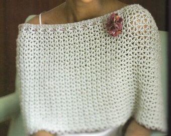 May include: Off-white crochet shawl with a delicate openwork design. The shawl features a decorative edge and a small, dark pink flower pinned near the shoulder. The garment is lightweight and appears to be handmade.