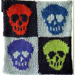 May include: A knitted square featuring four skull designs in a grid pattern. Each skull is a different color: red, blue, purple, and green. The background alternates between black and light gray.