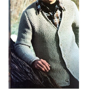 May include: A light green, textured cardigan sweater with button closures. The sweater has a V-neck and long sleeves. The person is wearing a plaid shirt underneath the sweater.