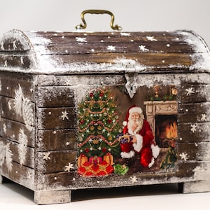 May include: A wooden Christmas chest with a curved top, featuring a festive scene of Santa Claus, a decorated Christmas tree, and a fireplace. The chest is painted brown with white accents and a brass handle.