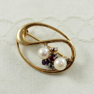 Peut inclure: Une broche dorée à la forme ovale unique ornée de deux perles blanches et d'un groupe de pierres précieuses colorées.