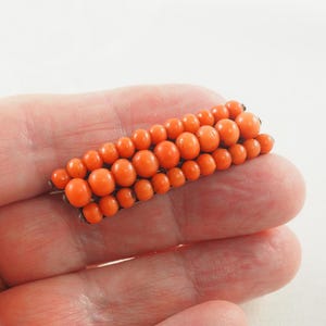 May include: A vintage coral brooch with a rectangular shape, made of small, round coral beads in a vibrant orange color.