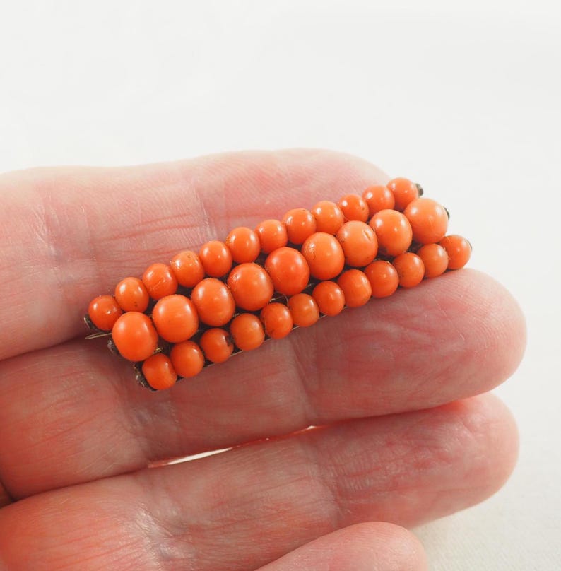 May include: A vintage coral brooch with a rectangular shape, made of small, round coral beads in a vibrant orange color.