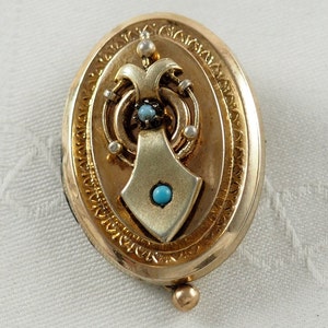 K&ouml;nnte beinhalten: Ovales goldenes Medaillon mit einem detaillierten Design mit einer T&uuml;rkis- und Perlenverzierung.