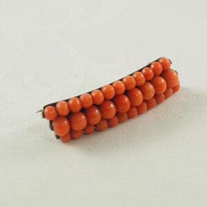 May include: A vintage brooch made of coral beads in a graduated size, set in a gold tone metal.