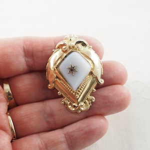 Peut inclure: Un pendentif en or avec un camée blanc orné d'une étoile rouge au centre. Le pendentif est en forme de diamant et présente des détails complexes.