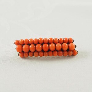 May include: A vintage brooch made of orange coral beads arranged in three rows.